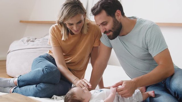 Loving Parents With Newborn Baby Lying On Bed At Home In Loft Apartment