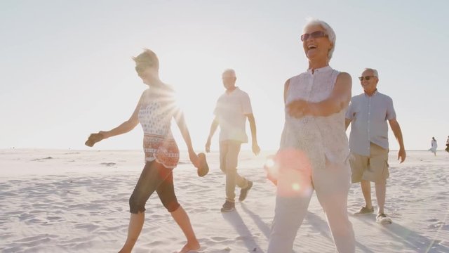 Group Of Senior Friends Walking Along Sandy Beach On Summer Group Vacation 