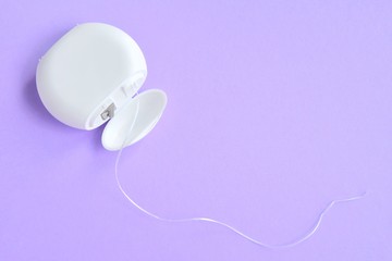Dental floss in white plastic box with selective focus on purple background with empty space for...