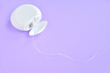 Dental floss in white plastic box with selective focus on purple background with empty space for...