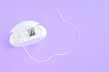 Dental floss in white plastic box with selective focus on purple background with empty space for image or text. White hygienic dental floss for daily routine healthcare on neutral backdrop. Dentistry 