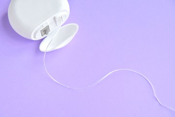Dental floss in white plastic box with selective focus on purple background with empty space for image or text. White hygienic dental floss for daily routine healthcare on neutral backdrop. Dentistry 