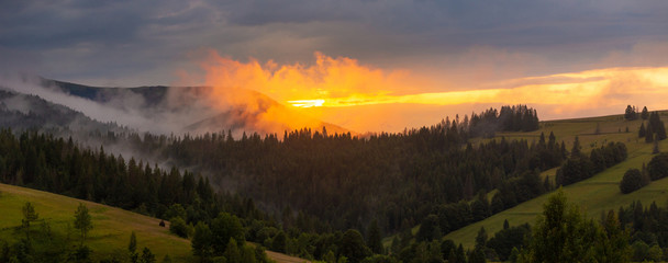 Bright sunset over foggy mountains. Vivid sun through the clouds over mountains slopes, covered...