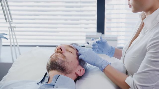 Female Beautician Giving Mature Male Patient Botox Injection In Forehead