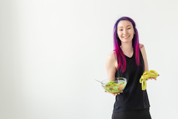 Unidentified young girl hipster with purple hair measures her waist with a measuring tape on a white background with copyspace. Healthy lifestyle concept.