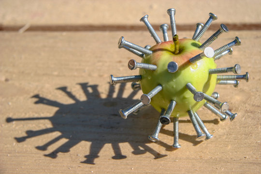 Green with red apple with stuck nails lies on a wooden bar on a sunny day. Abstraction. Hellraiser. Raw timber. Selective focus.