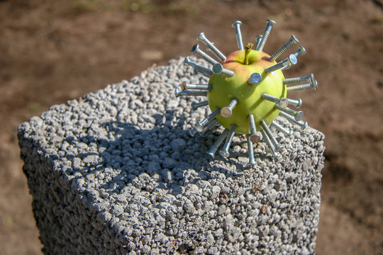 A green apple with nails stuck like a head in a film Hellraiser lies on a block on a sunny day. Abstraction. Selective focus. Brown blurred background.