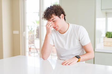 Young handsome man wearing white t-shirt at home tired rubbing nose and eyes feeling fatigue and headache. Stress and frustration concept. © Krakenimages.com