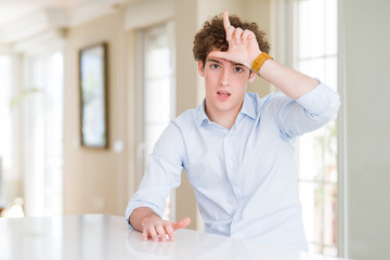 Young business man with curly read head making fun of people with fingers on forehead doing loser...
