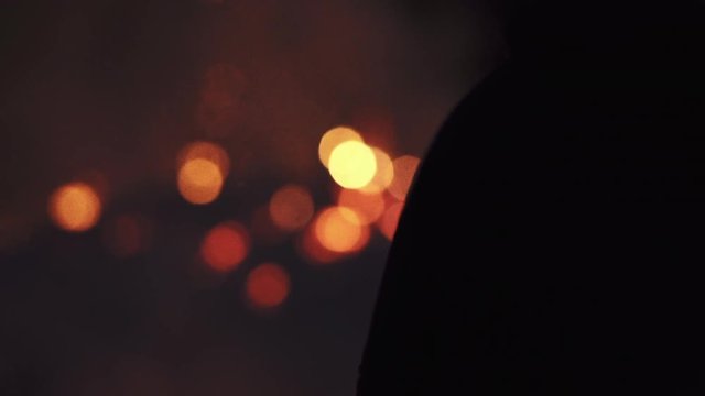 Anonymous silhouettes of people standing around a big bonfire burning at night. Short handheld artistic shot with bokeh and shadows.