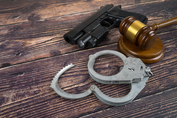 Obraz premium Judge gavel, pistol and handcuffs on wooden background. Concept court, law, approach and punishment