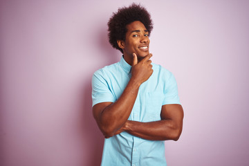 Young american man with afro hair wearing blue shirt standing over isolated pink background looking confident at the camera smiling with crossed arms and hand raised on chin. Thinking positive.