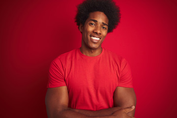 Fototapeta na wymiar Young american man with afro hair wearing t-shirt standing over isolated red background happy face smiling with crossed arms looking at the camera. Positive person.
