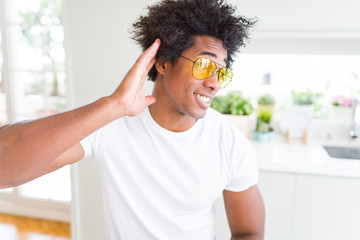 African American man wearing glasses smiling with hand over ear listening an hearing to rumor or gossip. Deafness concept.