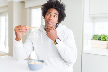 Fototapeta na wymiar African American man eating asian noodles using chopsticks at home serious face thinking about question, very confused idea