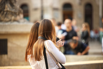 Young long-haired brown-haired girls walk in the center of the ancient city. Fashion of modern youth. Free time and happy weekend. Blurred background. Ancient architecture and design of buildings