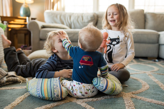 Rear View of Happy Young Siblings Playing with Baby Brother at Home
