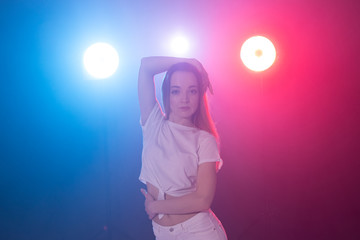 Nightlife and club concept - young woman dancing in the dark under the lights
