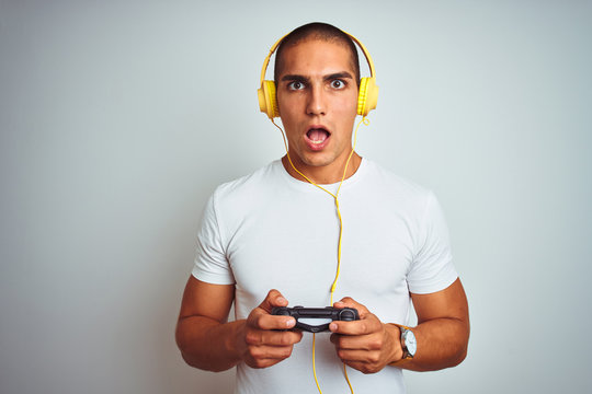 Young handsome man playing videogames using headphones over white isolated background scared in shock with a surprise face, afraid and excited with fear expression