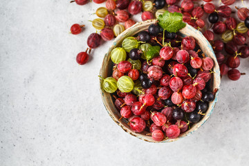 Red, green and black gooseberries in a bowl on gray background, top view.