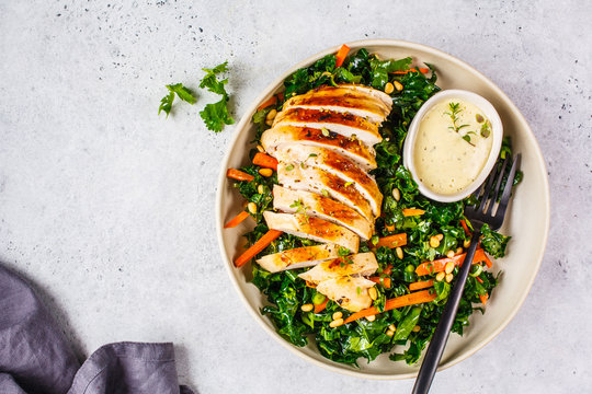 Grilled chicken breast salad with kale, pine nuts and caesar dressing in a white plate.