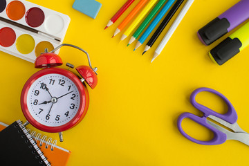 School stationery and red alarm clock on the yellow background.Top view. Copy space.