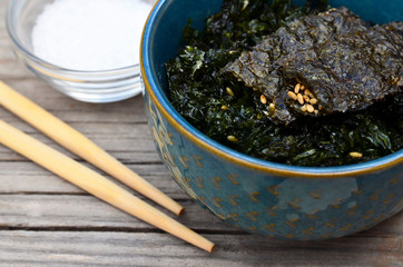 Salty roasted dried seaweed nori with sesame seeds in a blue bowl on old wooden table.Healthy snack,Korean food concept.