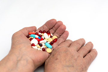 Old hands hold multicolored medical pills and tablets for ingestion from diseases on a white background.