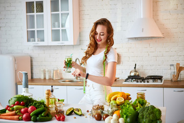 Young woman drinking fresh water with cucumber, lemon and leaves of mint from glass in the kitchen. Healthy Lifestyle and Eating. Health, Beauty, Diet Concept.