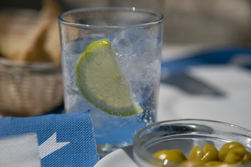 Vaso de refrescante bebida con limón y aperitivo de olivas