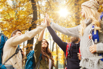 travel, tourism and hike concept - group of friends or travelers with backpacks making high five over autumn park background