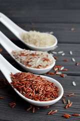 Different types of rice in spoons on wooden table background