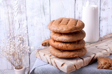 Stack of round brown rye flatbread on the white wooden background. Bottle of milk in the background