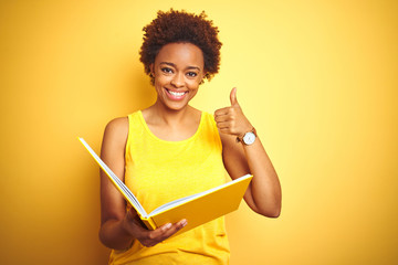 African american woman reading a book over yellow isolated background happy with big smile doing ok...