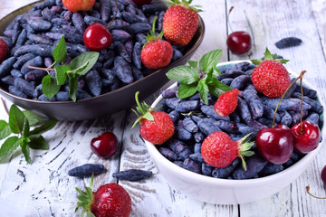 Honeysuckles, strawberries and cherries in white bowl on the table. Freshly picked berries