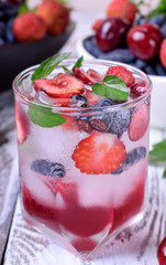 Lemonade with cherries, honeysuckles, strawberries, red syrup and ice in a glass topped with mint on the white table