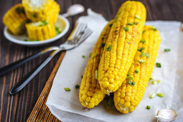 Grilled sweet corn cob under melting butter and greens on baking paper