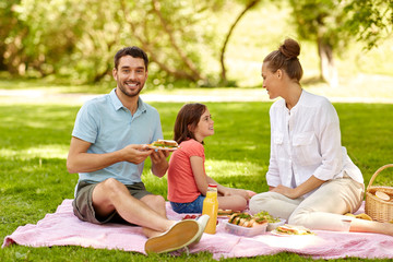 family, leisure and people concept - happy mother, father and daughter having picnic at summer park