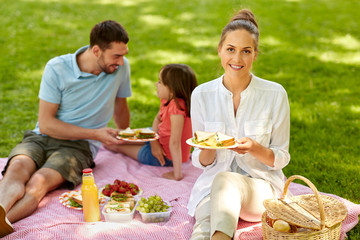 family, leisure and people concept - happy mother, father and daughter having picnic at summer park