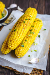 Grilled sweet corn cob under melting butter and greens on baking paper