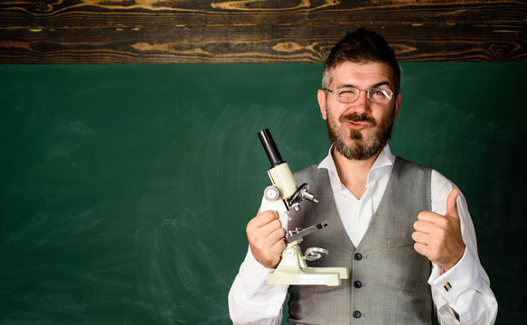 Teacher with microscope shows thumb up. Stem education. Education, school, teaching. Biology or chemistry science. Student in classroom shows ok gesture. Winking teacher near blackboard. Copy space.