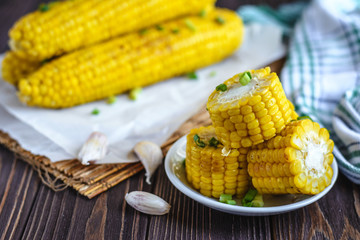 Grilled sweet corn cob under melting butter and greens on baking paper