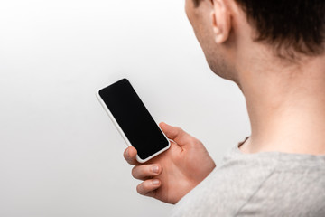 cropped view of man holding smartphone with blank screen isolated on grey