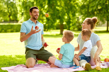 Fototapeta premium family, leisure and people concept - happy mother, father juggling apples and two little sons having picnic at summer park