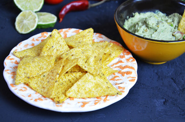 Mexican corn chips nachos with salsa dip on a black background with guacamole sauce, avacoda with lime and hot pepper