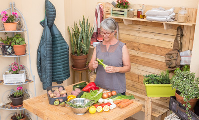 One senior woman smiling preparing vegetables for dinner. Table and background made by recycled wood. One caucasian people  with gray hair. Outdoor in terrace