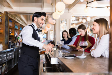 Fototapeta premium Barman is servicing young people who are relaxing in bar indoor.