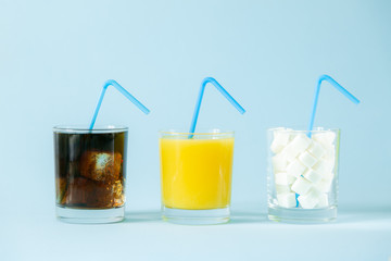 Excessive sugar consumption concept - cola, juice and sugar cubes in glasses on blue background,...