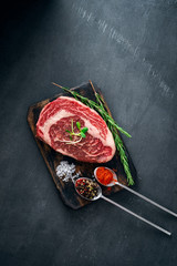 Marble raw Ribeye Steak with seasonings and red pepper on cutting Board on grey background, top view