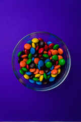 Bowl filled with multicolor candy on a purple background.